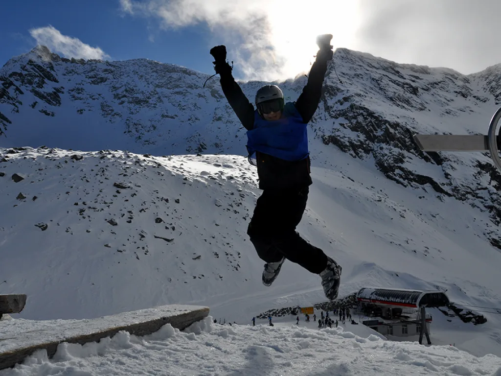Person springt vor einer Bergkulisse in die Luft.